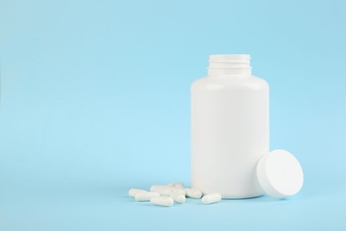 Photo of Blank white jar with vitamin capsules on light blue background, space for text