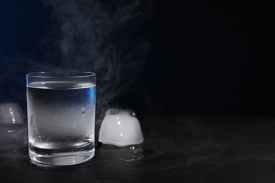 Photo of Vodka in shot glass with ice on black table against dark background, space for text