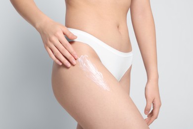 Photo of Woman applying body cream onto hip on light grey background, closeup