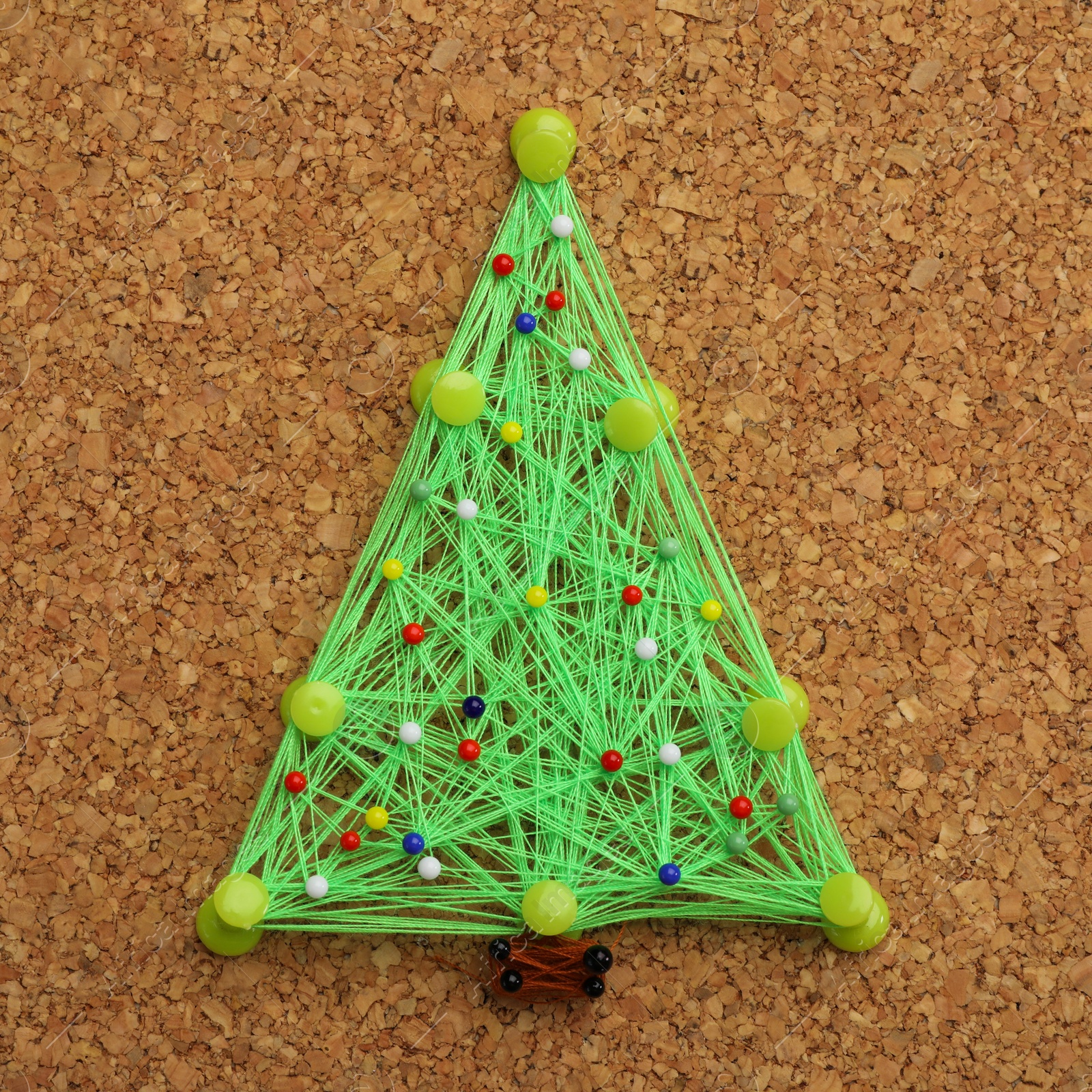 Photo of Christmas tree made of thread and pins on cork board. String art