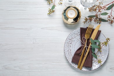 Stylish table setting with cutlery, burning candle and eucalyptus leaves, flat lay. Space for text