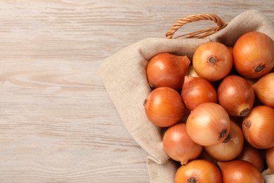 Photo of Wicker basket with many ripe onions on wooden table, top view. Space for text