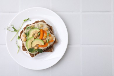 Tasty vegan sandwich with avocado, chickpeas and bell pepper on white tiled table, top view. Space for text