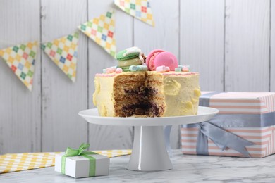 Delicious cake decorated with macarons and marshmallows and gift boxes on white marble table