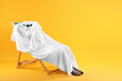 Photo of Person in ghost costume and sunglasses relaxing on chaise longue against yellow background, space for text