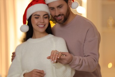 Photo of Making proposal. Happy woman with engagement ring and her fiance at home on Christmas, selective focus