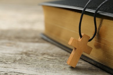 Photo of Christian cross and Bible on wooden table, closeup. Space for text