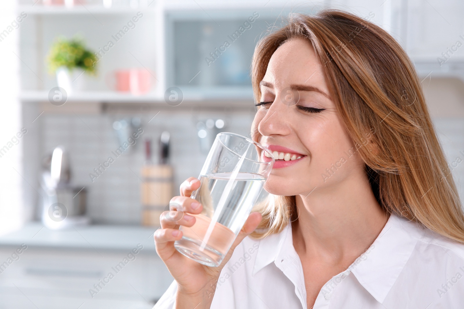 Photo of Young woman drinking clean water from glass in kitchen