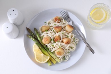 Delicious scallop pasta with asparagus, green onion and lemon served on white table, flat lay