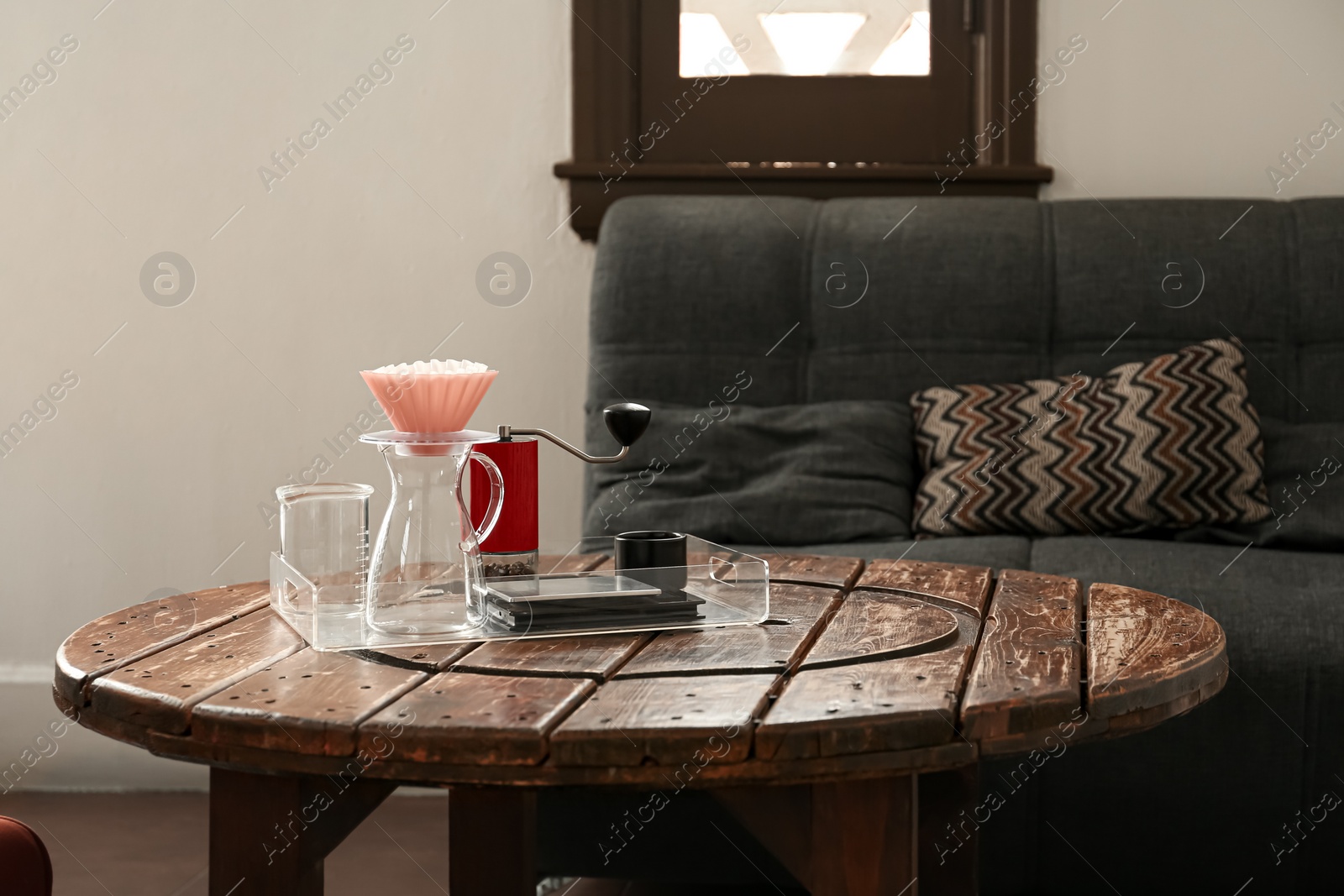 Photo of Manual coffee grinder with beans, glass jug and wave dripper on wooden table in cafe