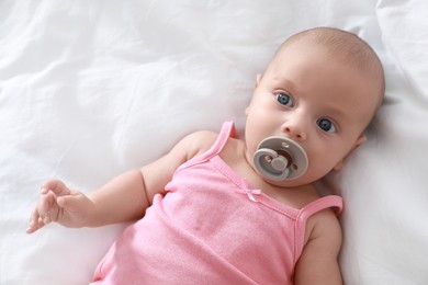 Photo of Cute little baby with pacifier lying on bed, top view