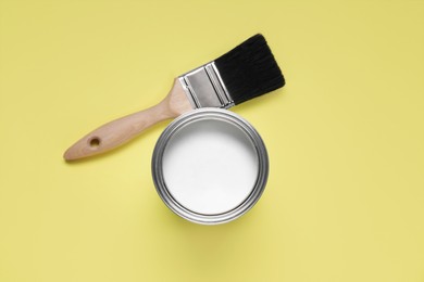 Can with white paint and brush on yellow background, flat lay