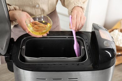 Photo of Woman spreading breadmaker pan with oil, closeup