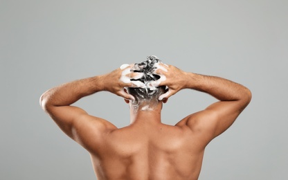 Photo of Man washing hair on grey background, back view