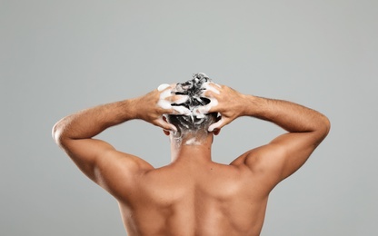 Man washing hair on grey background, back view