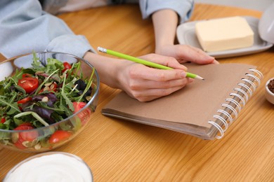 Woman with notebook and different products at wooden table, closeup. Keto diet