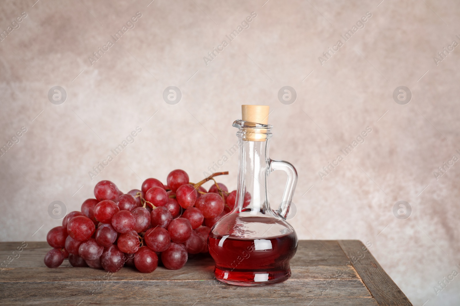 Photo of Glass jug with wine vinegar and fresh grapes on wooden table against color background