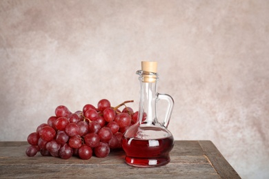 Photo of Glass jug with wine vinegar and fresh grapes on wooden table against color background