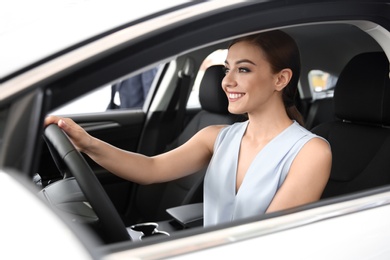 Young woman sitting in driver's seat of new car at salon