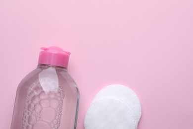 Photo of Micellar water and cotton pads on pink background, flat lay. Space for text