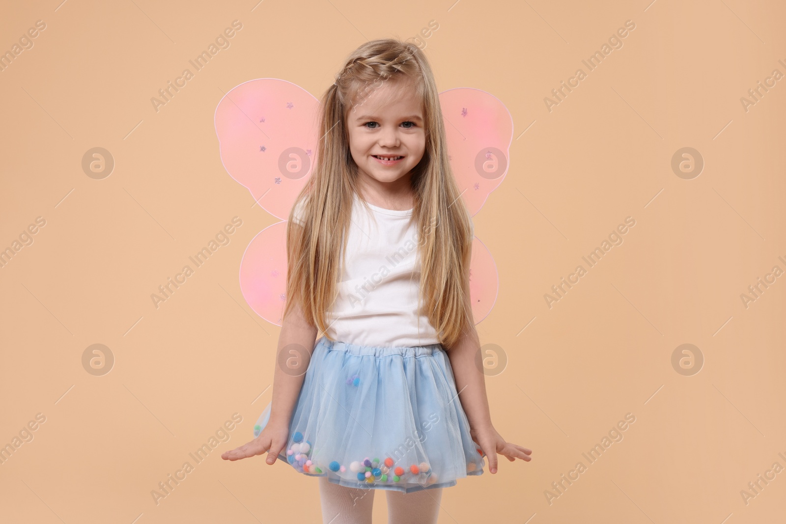 Photo of Cute little girl in fairy costume with pink wings on beige background