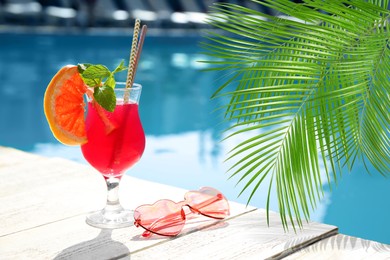 Image of View of beautiful green tropical leaves and cocktail with sunglasses near outdoor swimming pool on sunny day