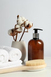 Photo of Different bath accessories and cotton flowers in vase on light table against white wall