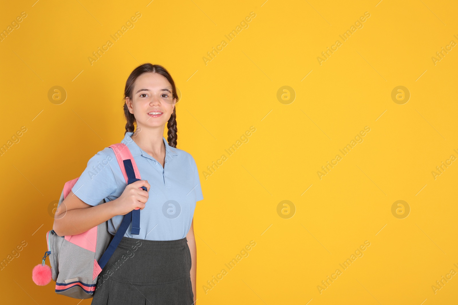 Photo of Teenage girl in school uniform with backpack on orange background, space for text