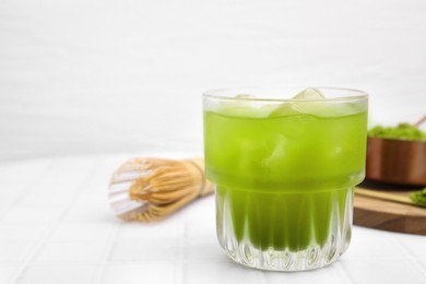 Photo of Glass of delicious iced green matcha tea on white tiled table, closeup. Space for text