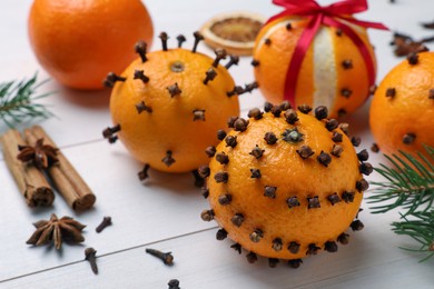 Photo of Pomander balls made of tangerines with cloves and fir branches on white wooden table, closeup