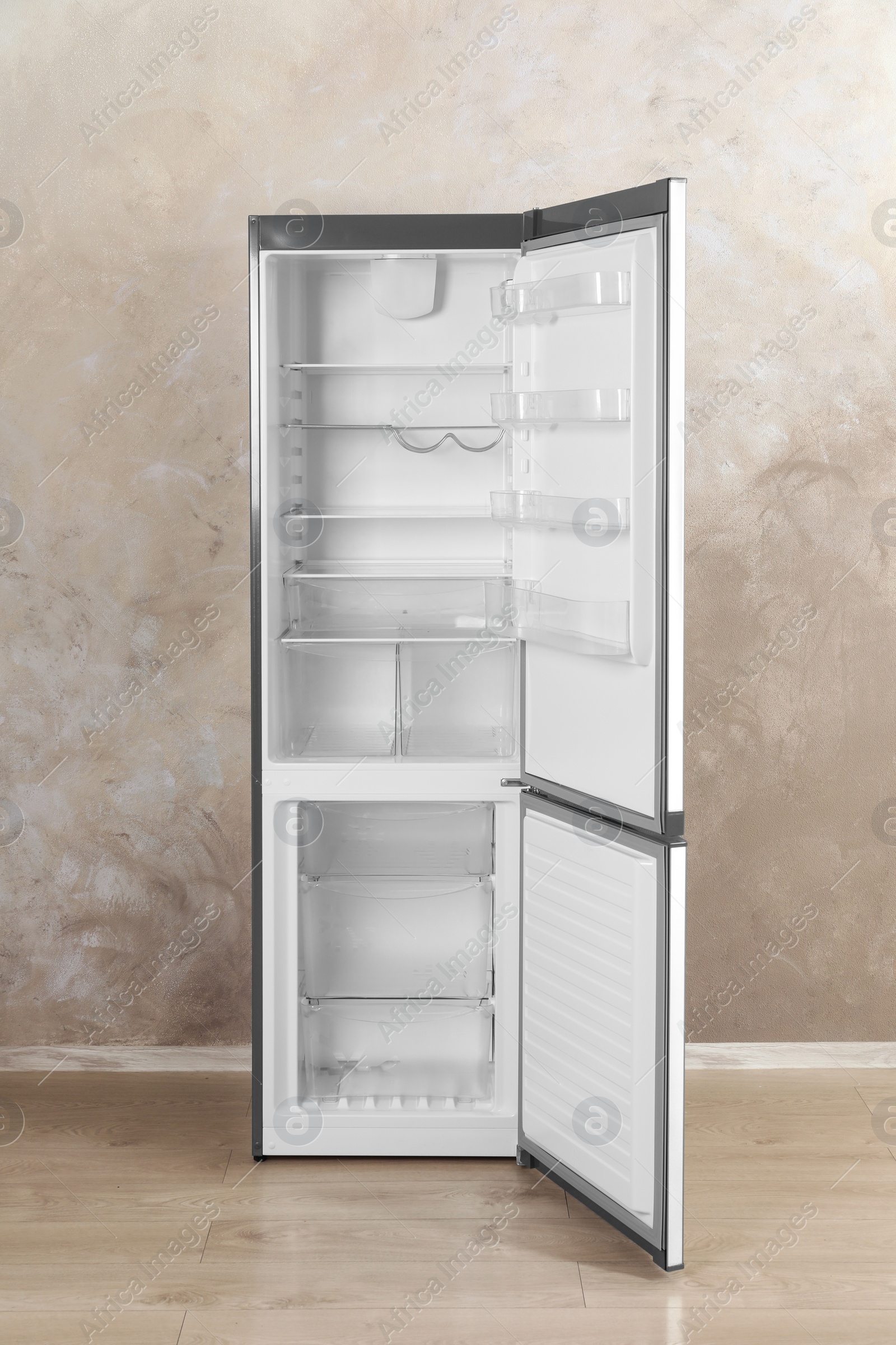 Photo of Open refrigerator with empty shelves near grey wall indoors