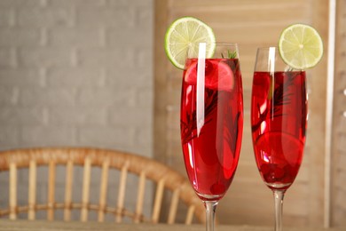 Tasty cranberry cocktail with rosemary and lime in glasses indoors, closeup. Space for text