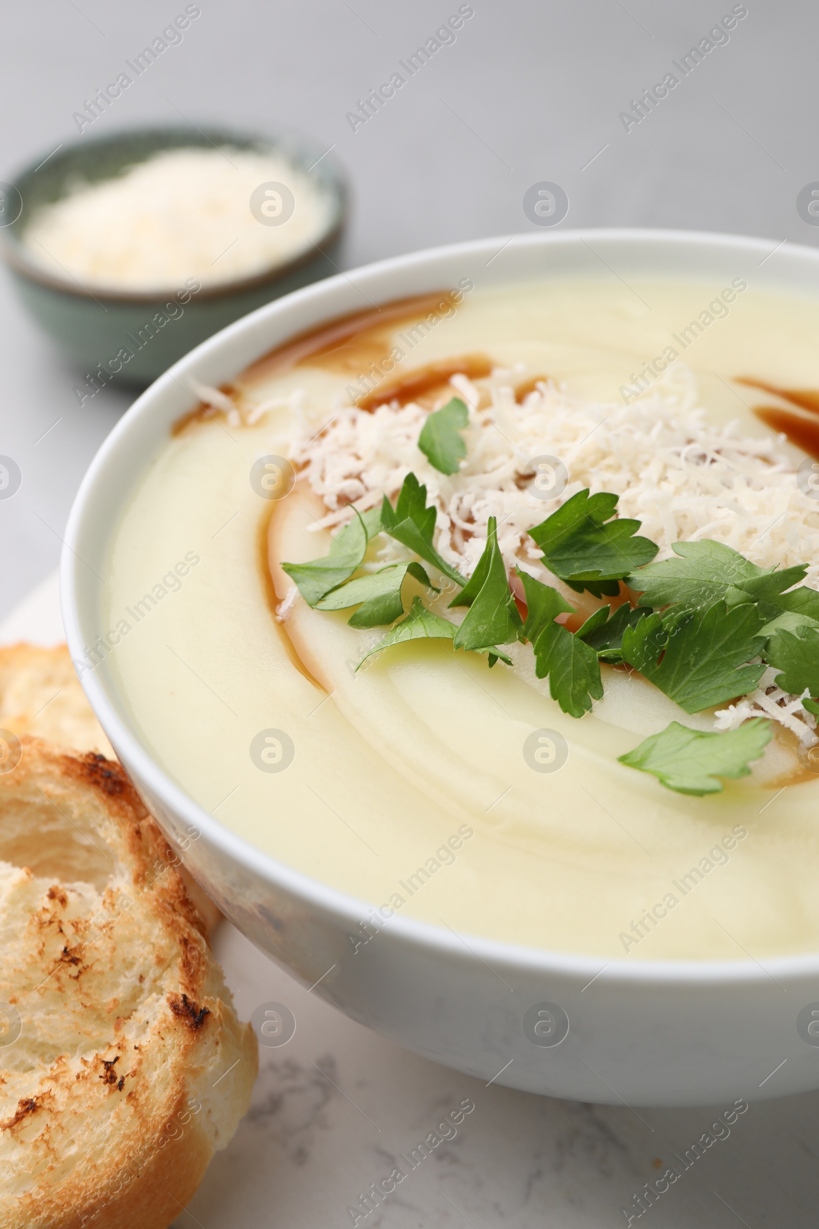 Photo of Delicious cream soup with parmesan cheese, soy sauce and parsley in bowl on light grey table, closeup