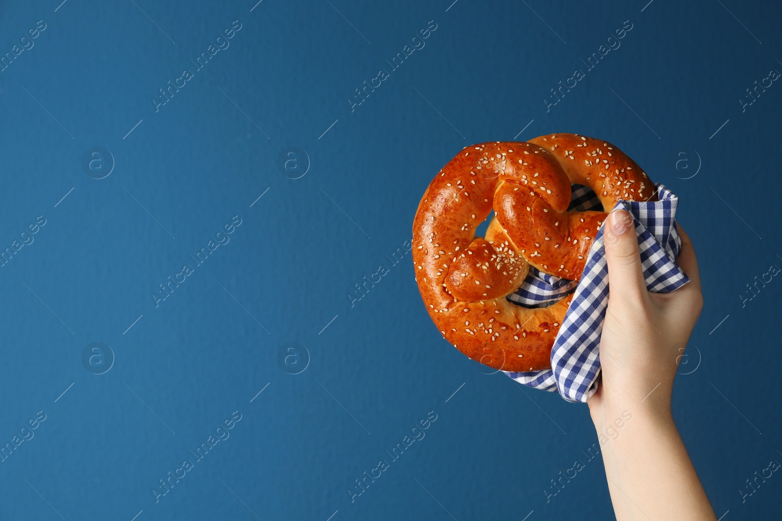 Photo of Woman with tasty freshly baked pretzel on blue background, closeup. Space for text