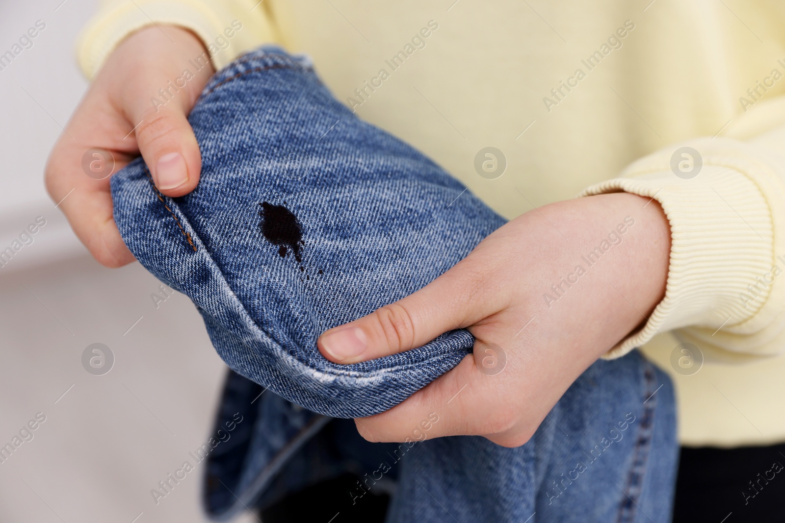 Photo of Woman holding jeans with black ink stain on blurred background, closeup