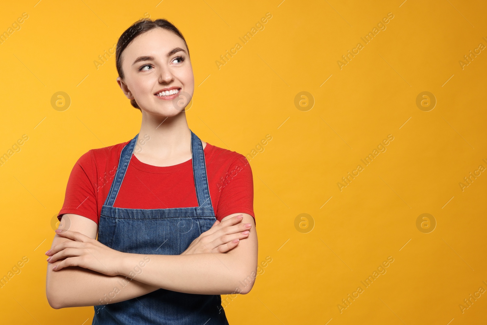 Photo of Beautiful young woman in clean denim apron on orange background. Space for text