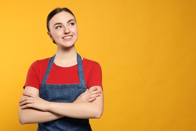 Beautiful young woman in clean denim apron on orange background. Space for text