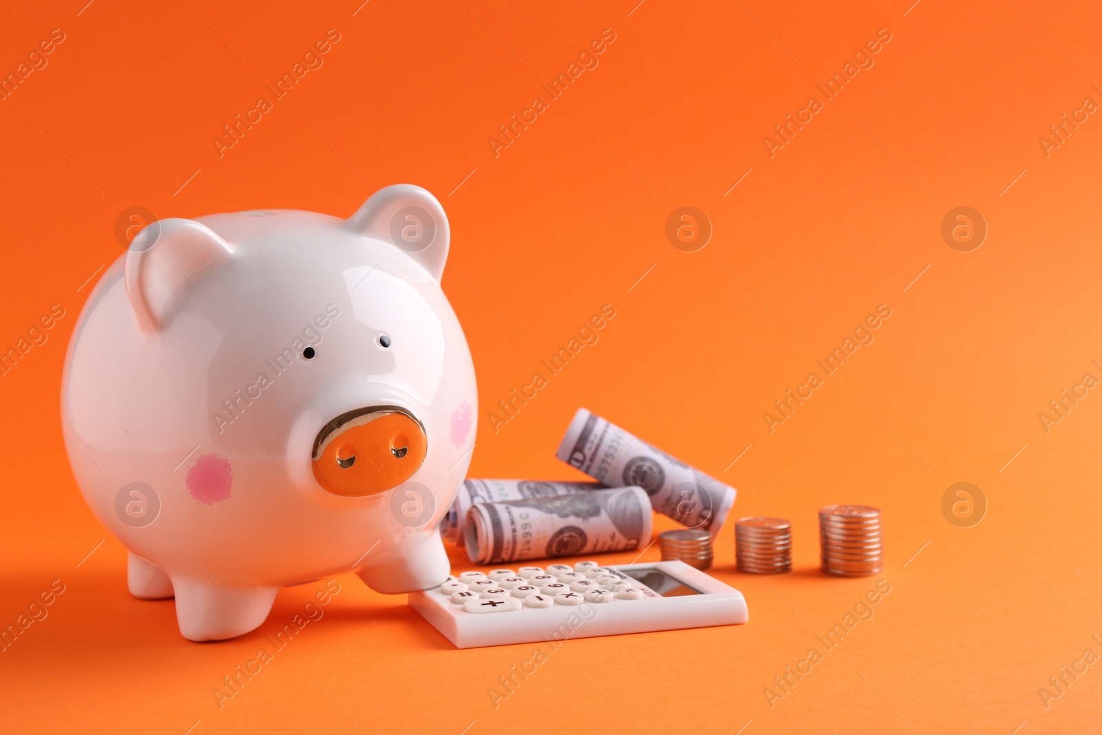 Photo of Financial savings. Piggy bank, dollar banknotes, coins and calculator on orange background