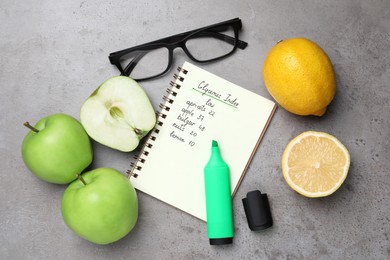 Photo of Notebook with products of low glycemic index, marker, glasses and fresh fruits on grey table, flat lay