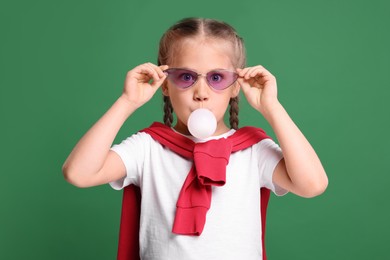 Photo of Girl in sunglasses blowing bubble gum on green background