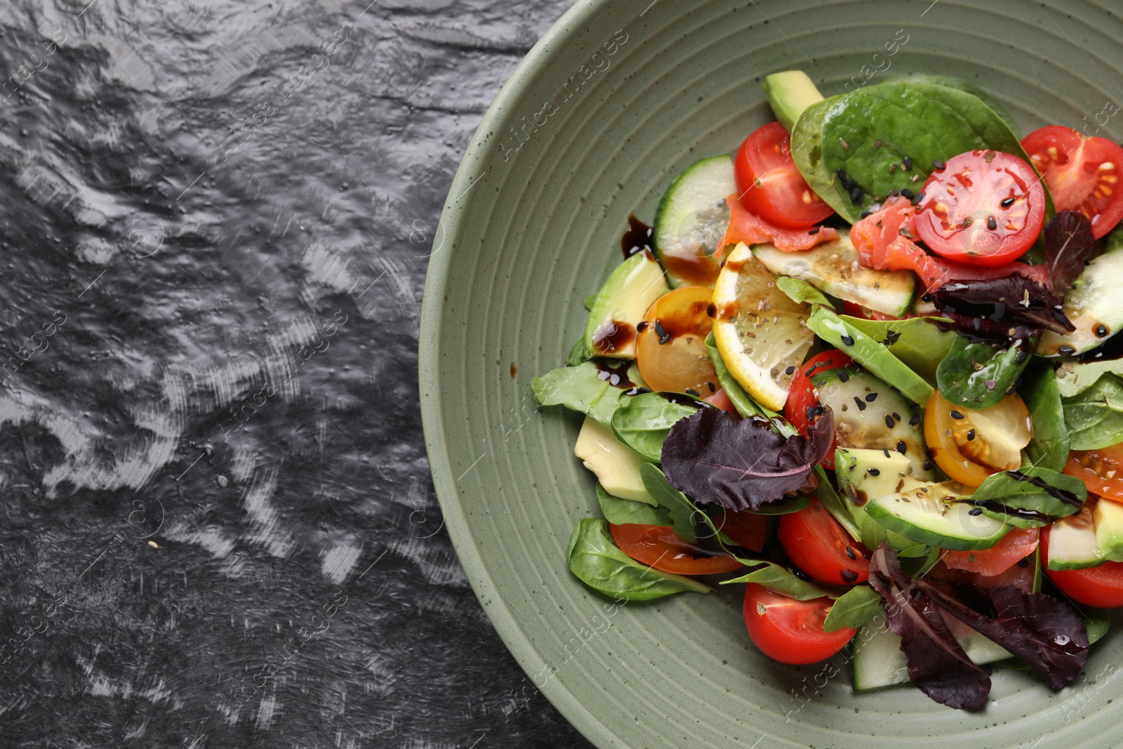 Photo of Delicious vegetable salad on black textured table, top view. Space for text