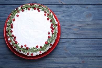 Traditional Christmas cake decorated with rosemary and cranberries on blue wooden table, top view. Space for text