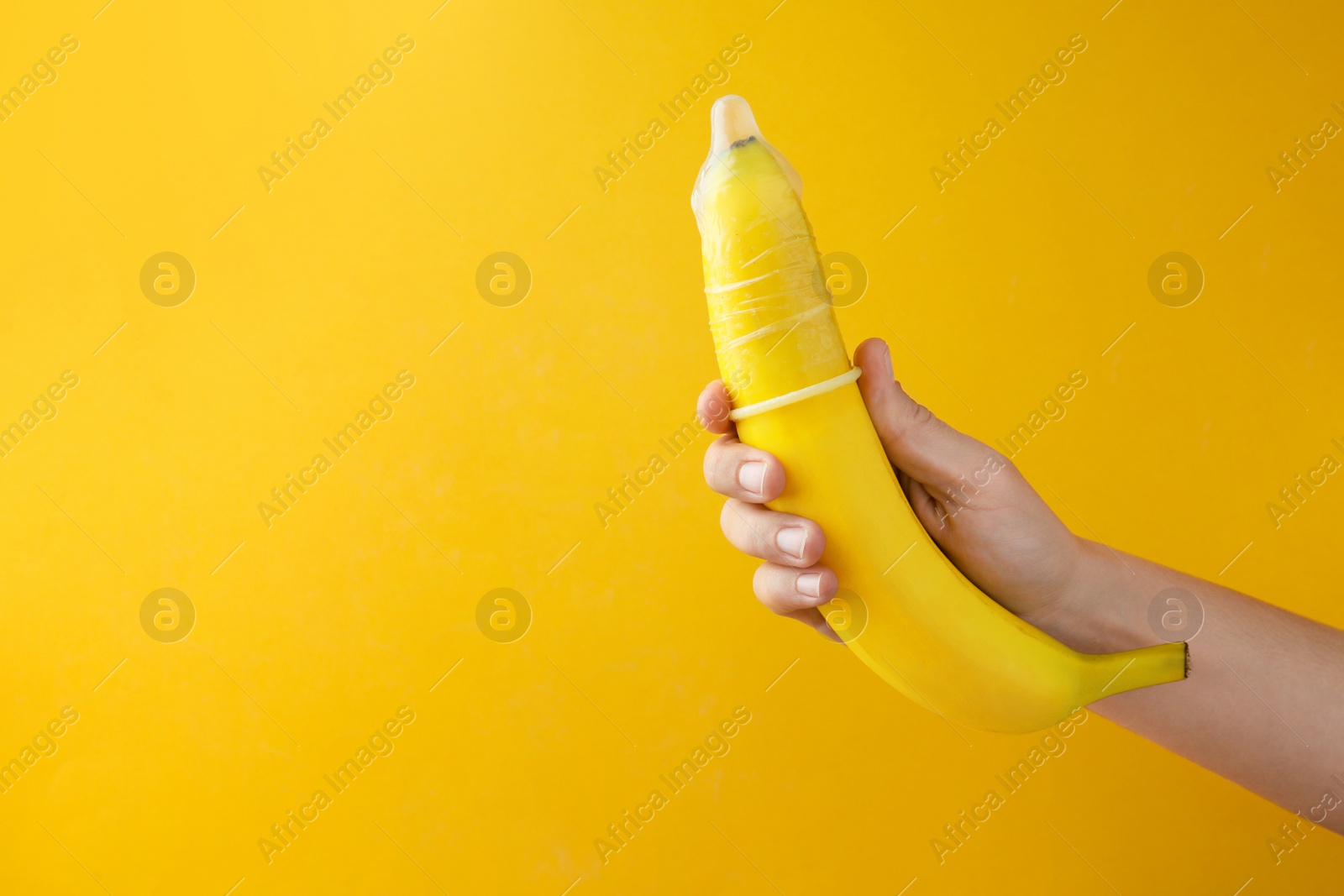 Photo of Woman holding banana in condom on orange background, closeup and space for text. Safe sex concept