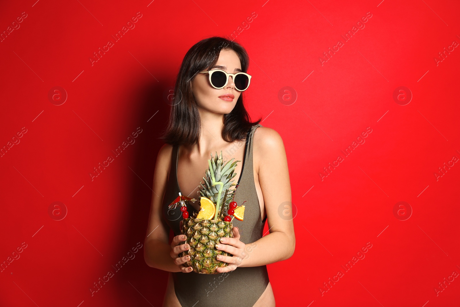 Photo of Beautiful woman in stylish swimsuit holding tropical cocktail on red background