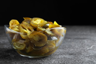 Glass bowl with slices of pickled green jalapeno peppers on grey table, space for text