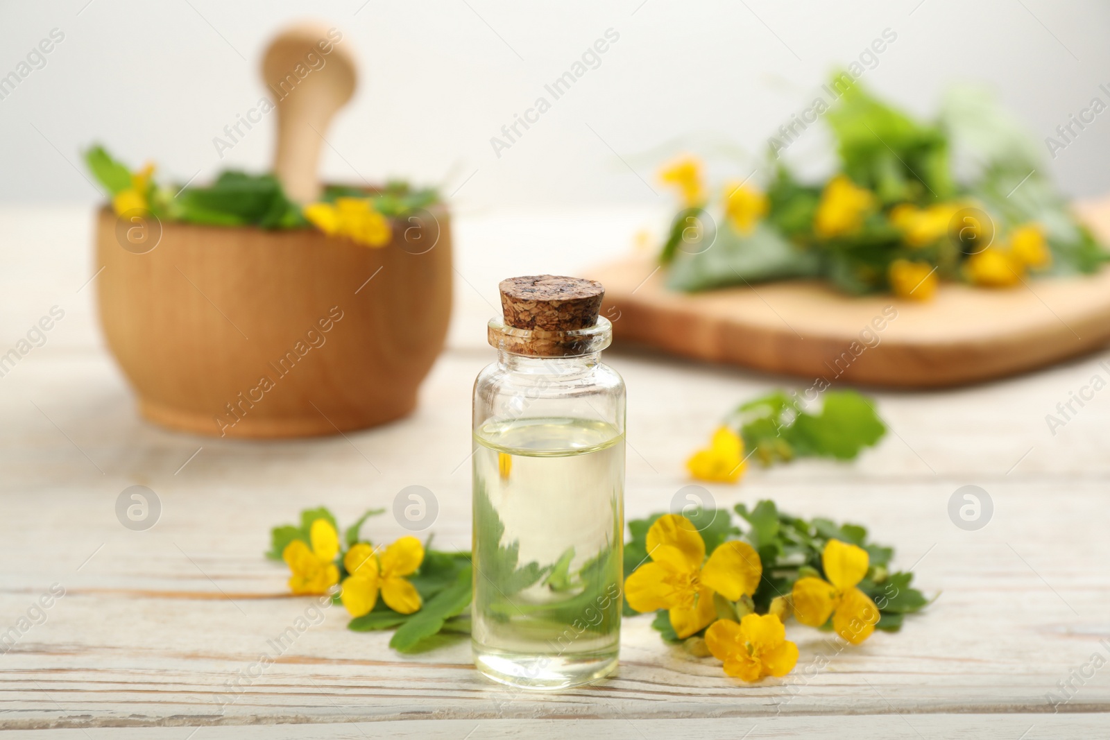 Photo of Bottle of natural celandine oil near flowers on white wooden table