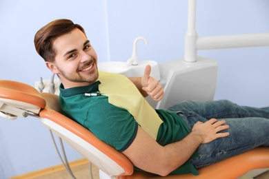 Happy patient on dentist's chair in modern clinic, space for text