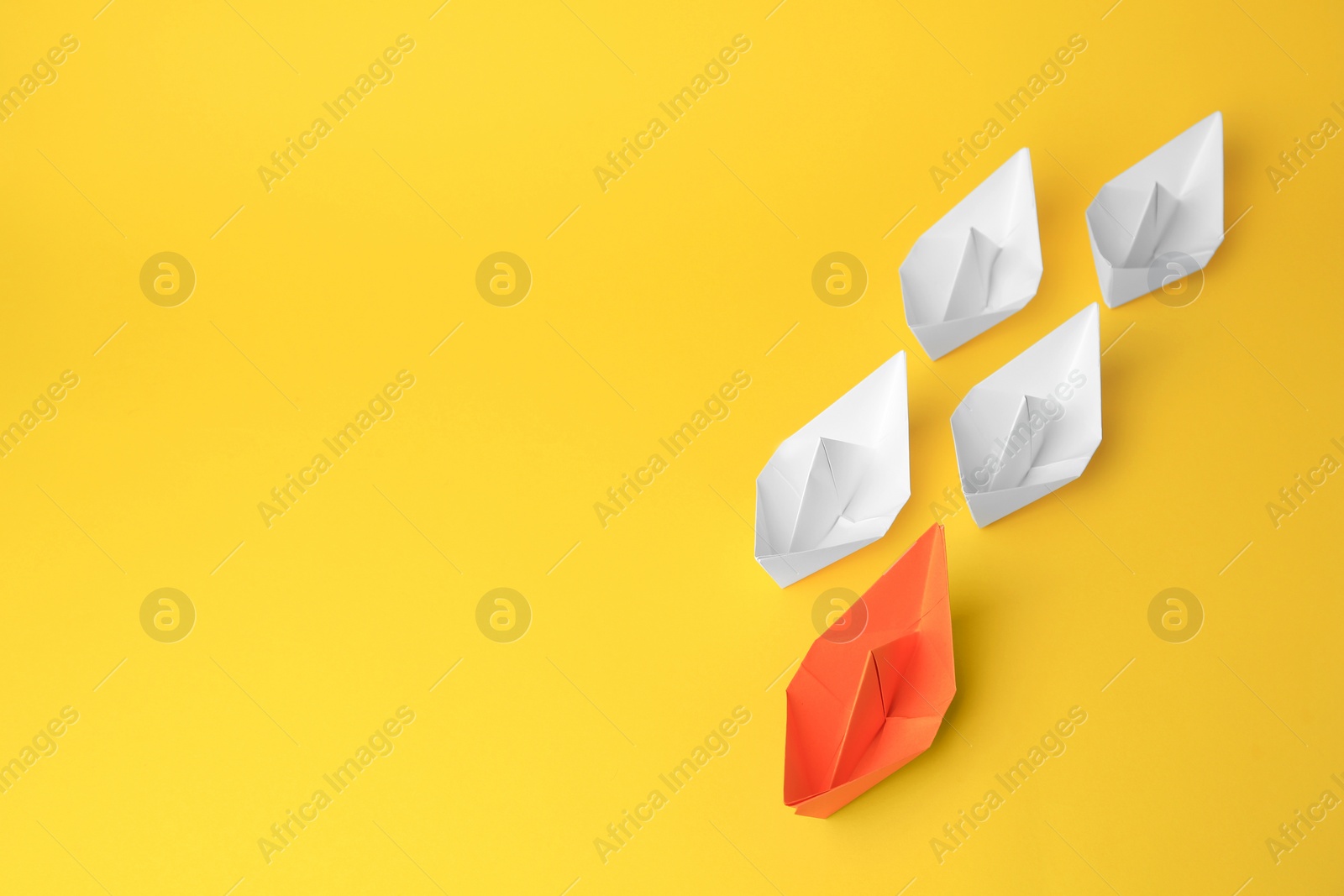 Photo of Group of paper boats following orange one on yellow background, space for text. Leadership concept