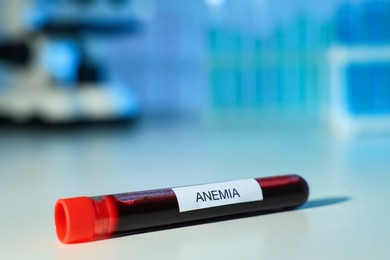 Test tube with blood sample and label Anemia on white table against blurred background, closeup. Space for text