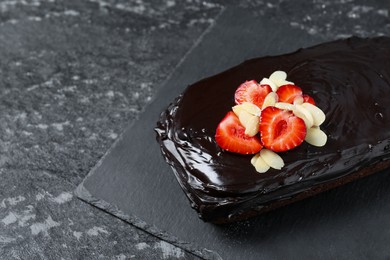Photo of Delicious chocolate sponge cake with strawberry and almond flakes on black table, closeup. Space for text